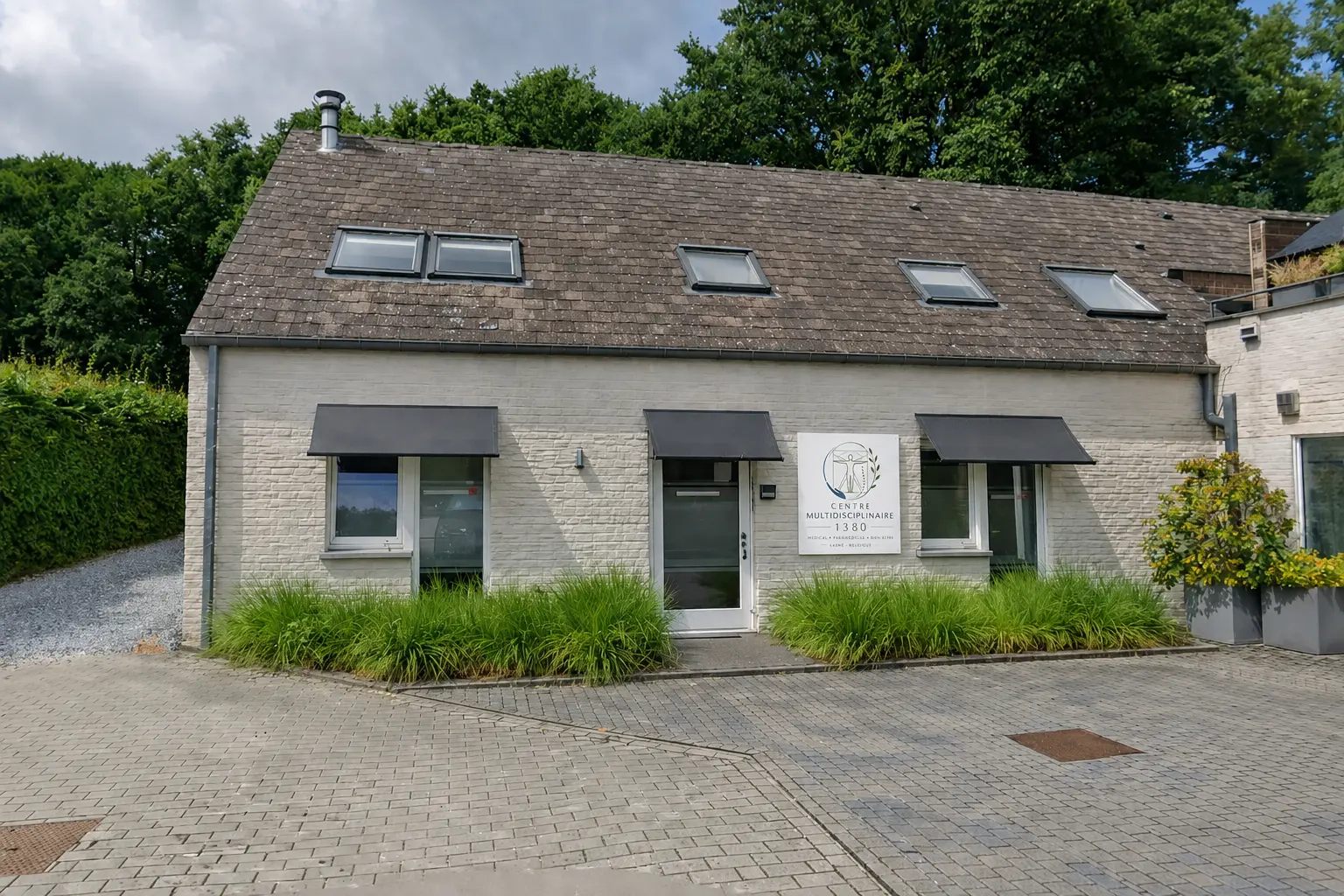 Façade du Centre Multidisciplinaire 1380 à Lasne, bâtiment en briques claires avec auvents foncés et verdure environnante